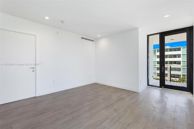 unfurnished room featuring a wall of windows, light wood-type flooring, baseboards, and recessed lighting