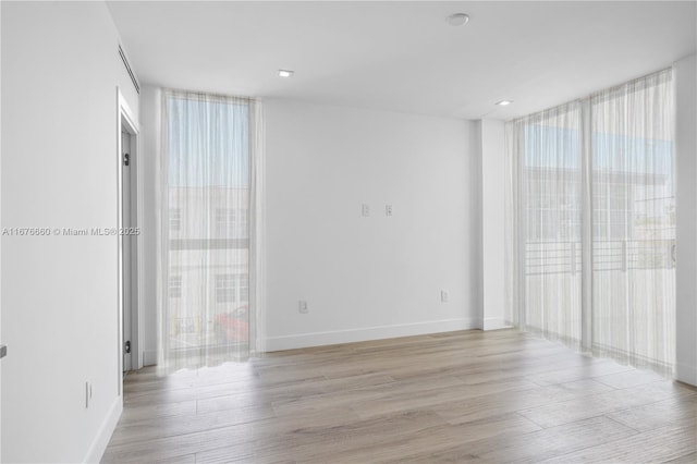 unfurnished room featuring light wood-style floors, baseboards, and a wall of windows