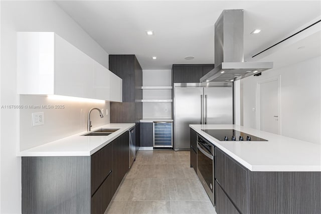 kitchen with island range hood, modern cabinets, appliances with stainless steel finishes, light countertops, and a sink