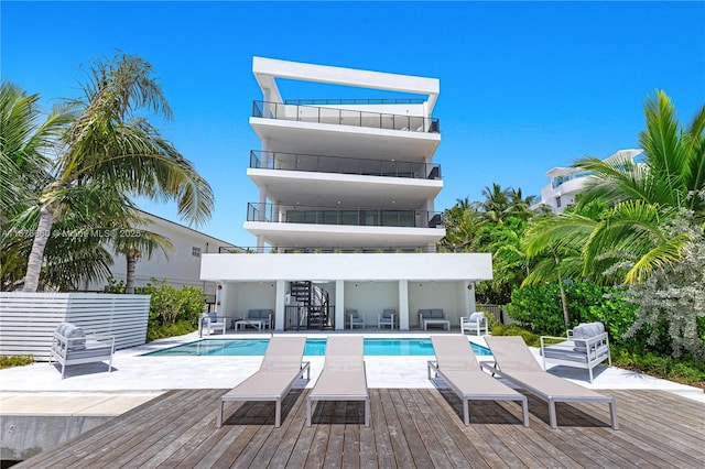 back of property featuring a deck, an outdoor pool, a balcony, and a patio