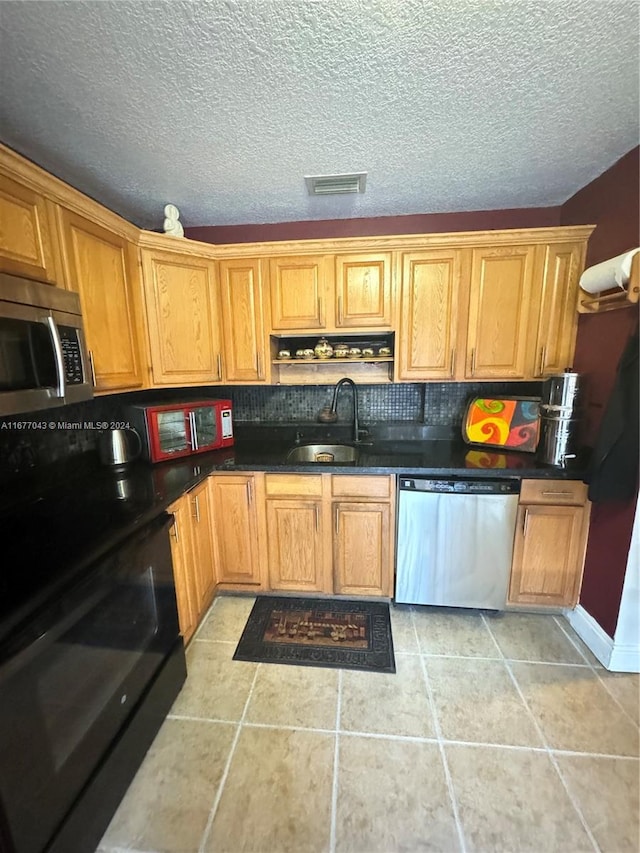 kitchen with decorative backsplash, sink, light tile patterned flooring, appliances with stainless steel finishes, and a textured ceiling