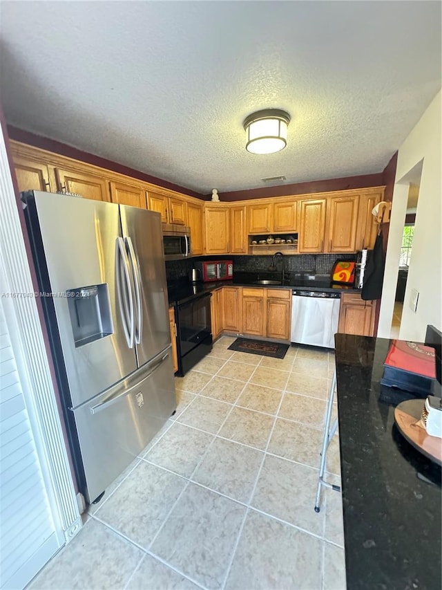 kitchen featuring decorative backsplash, light tile patterned floors, a textured ceiling, sink, and stainless steel appliances