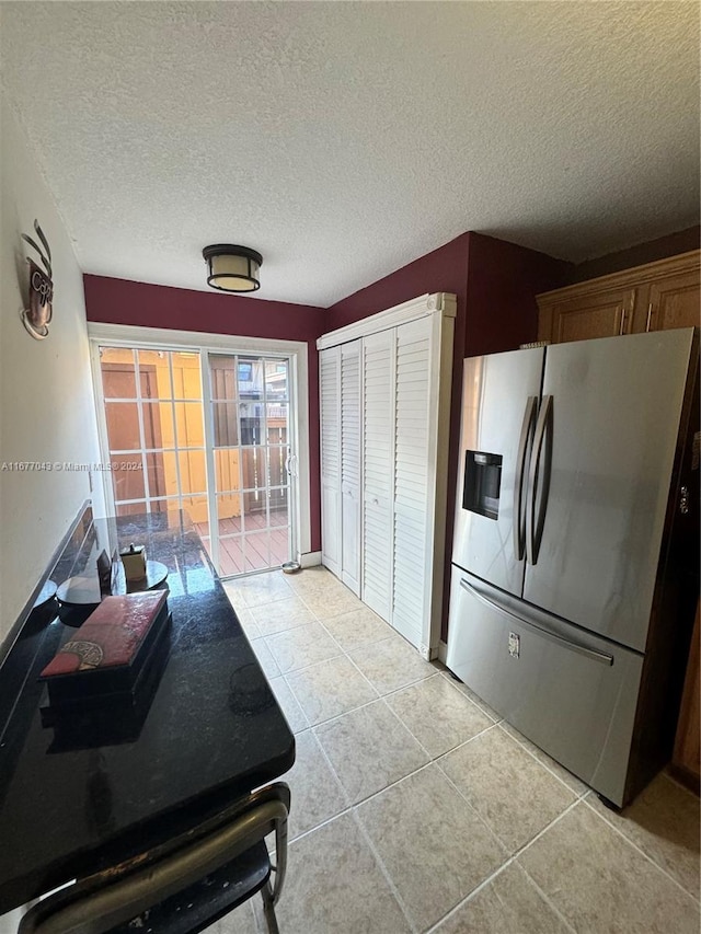 kitchen featuring stainless steel fridge, light tile patterned flooring, and a textured ceiling