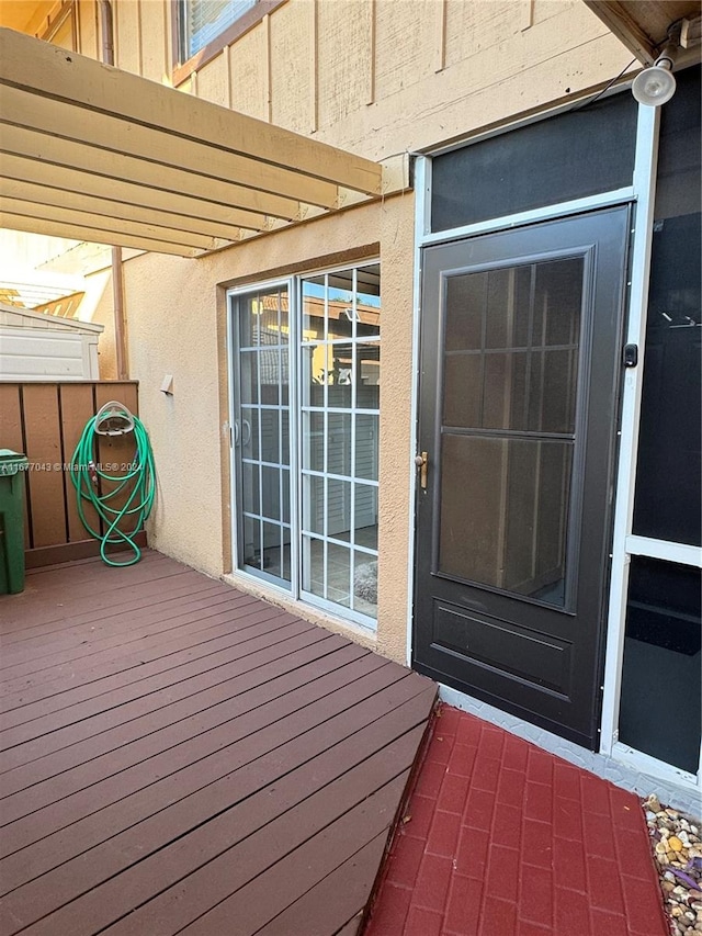 view of exterior entry featuring a deck and a pergola