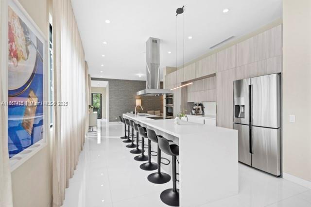 kitchen with sink, island exhaust hood, double oven, light tile patterned floors, and a kitchen island with sink