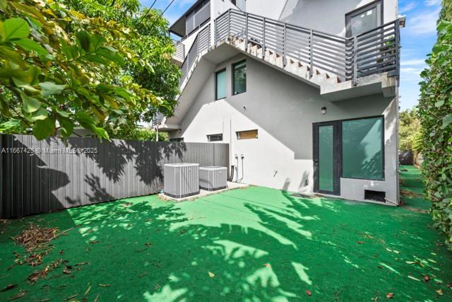 rear view of house with a balcony, a lawn, and central AC unit