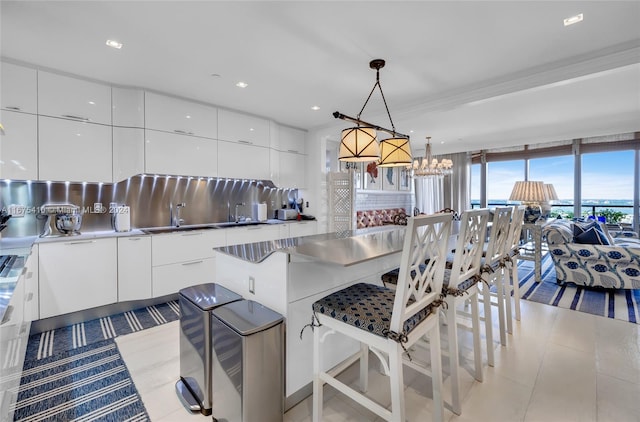 kitchen featuring a kitchen bar, pendant lighting, white cabinets, a notable chandelier, and decorative backsplash