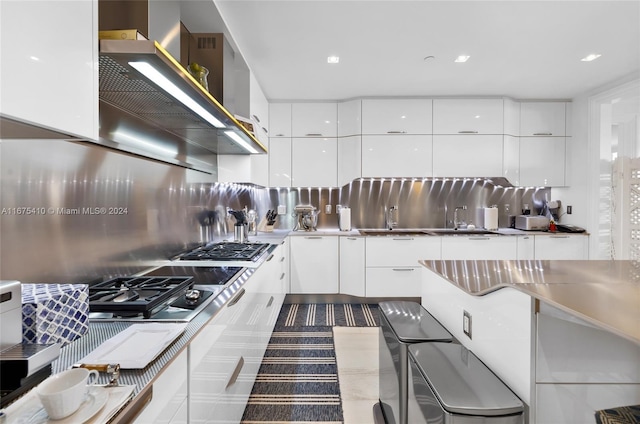 kitchen with stainless steel counters, sink, stainless steel gas stovetop, white cabinets, and tasteful backsplash