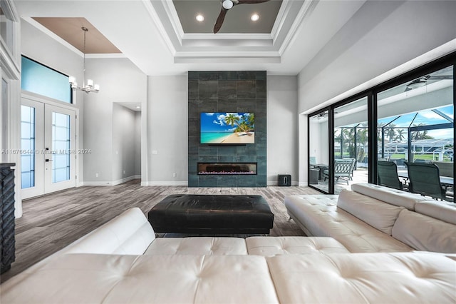 living room with a high ceiling, ceiling fan with notable chandelier, crown molding, wood-type flooring, and a tiled fireplace