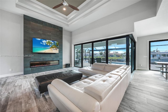 living room with ceiling fan, a raised ceiling, light hardwood / wood-style floors, a fireplace, and ornamental molding