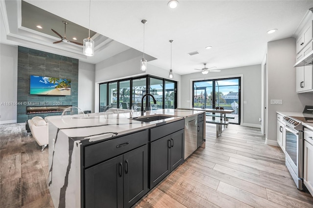 kitchen featuring stainless steel appliances, sink, decorative light fixtures, a center island with sink, and white cabinetry