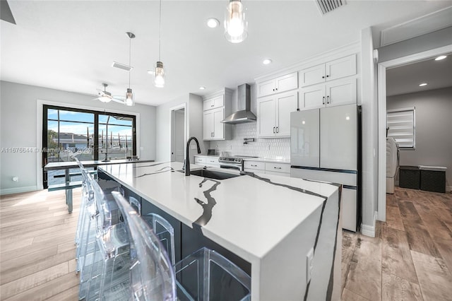 kitchen with white cabinetry, wall chimney exhaust hood, hanging light fixtures, stainless steel appliances, and light hardwood / wood-style floors