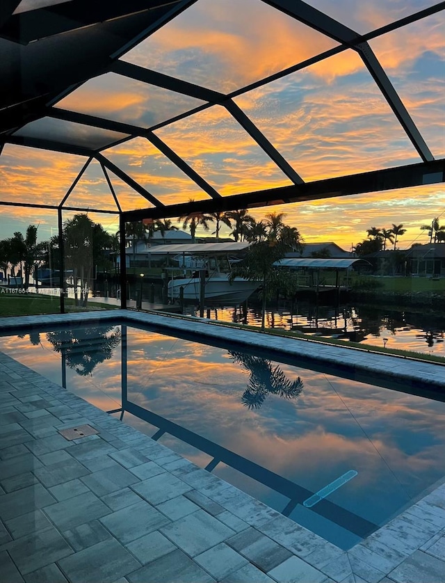 pool at dusk featuring glass enclosure and a patio area