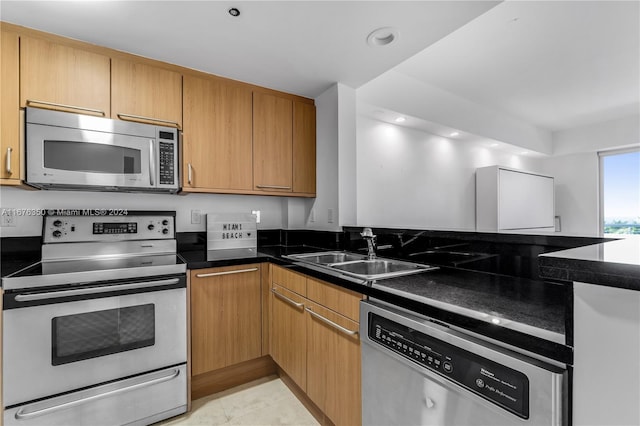 kitchen with appliances with stainless steel finishes, sink, dark stone counters, and light tile patterned floors