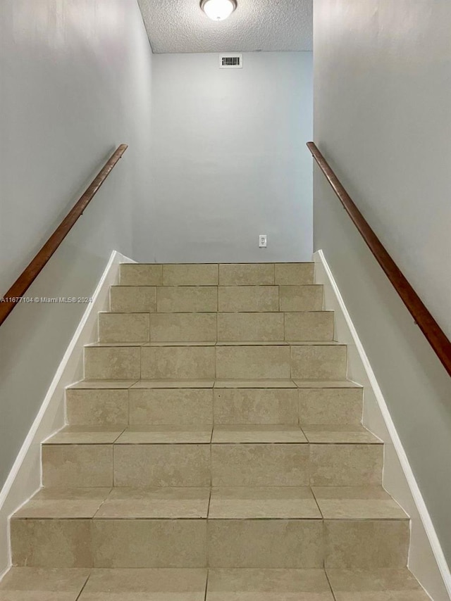 stairway with a textured ceiling and tile patterned floors