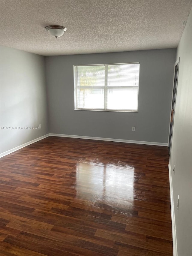 spare room featuring a textured ceiling and dark hardwood / wood-style floors