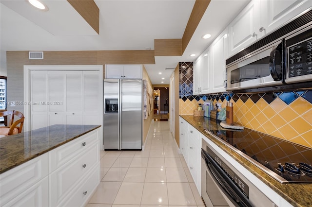 kitchen featuring white cabinets, decorative backsplash, dark stone countertops, light tile patterned floors, and stainless steel appliances