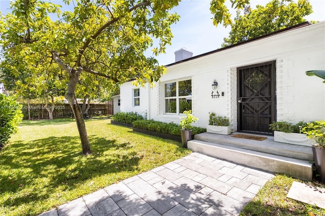 doorway to property with a lawn, a chimney, and fence