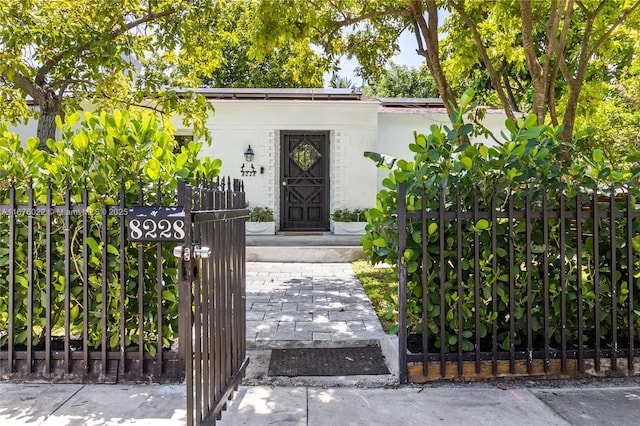 view of exterior entry featuring a gate, fence, roof mounted solar panels, and stucco siding