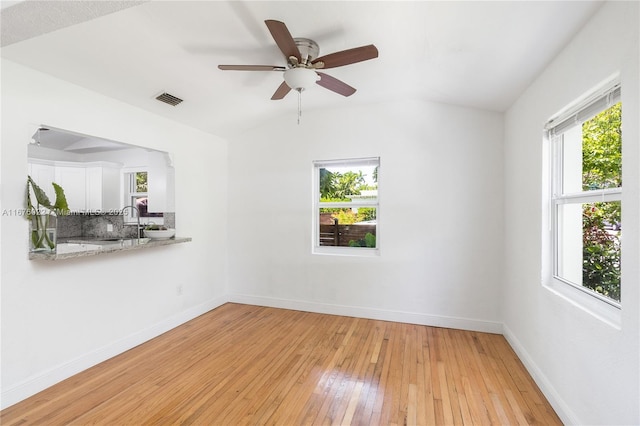 unfurnished room featuring light wood finished floors, visible vents, baseboards, vaulted ceiling, and a sink