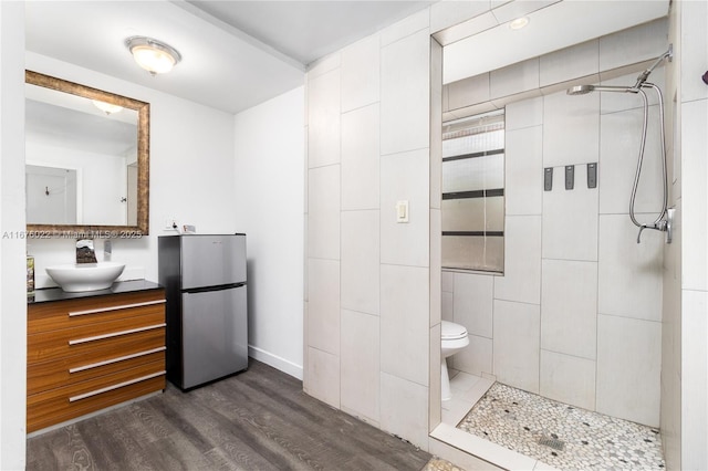 full bathroom with baseboards, tiled shower, toilet, wood finished floors, and vanity