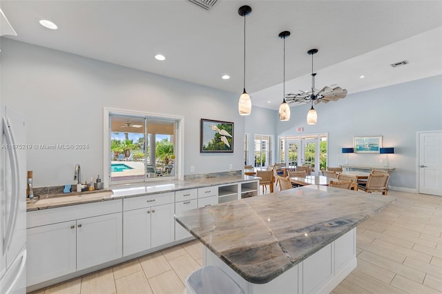 kitchen with a large island, white cabinetry, light stone counters, and plenty of natural light