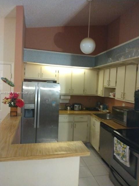 kitchen featuring cream cabinetry, hanging light fixtures, light tile patterned flooring, appliances with stainless steel finishes, and a textured ceiling