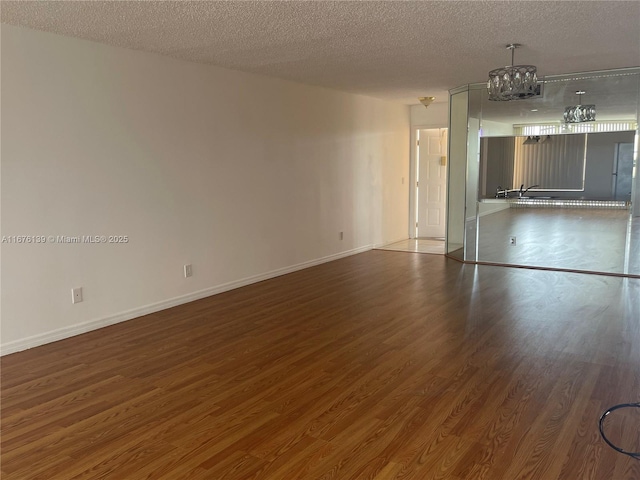 empty room featuring dark wood-type flooring, a textured ceiling, and an inviting chandelier