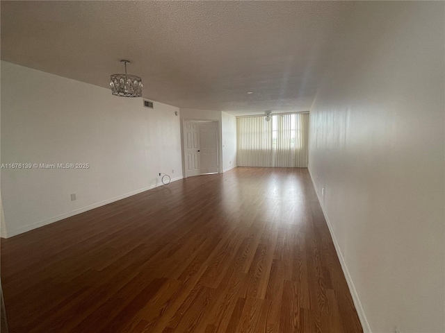 spare room featuring a textured ceiling, a chandelier, and dark hardwood / wood-style floors