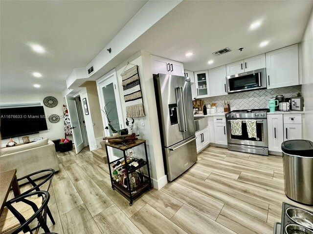 kitchen with decorative backsplash, white cabinetry, stainless steel appliances, and light wood-type flooring