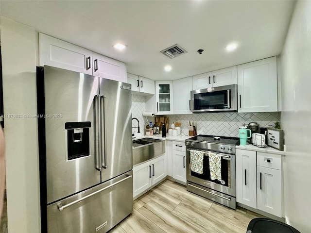 kitchen with white cabinets, light wood-type flooring, appliances with stainless steel finishes, and tasteful backsplash