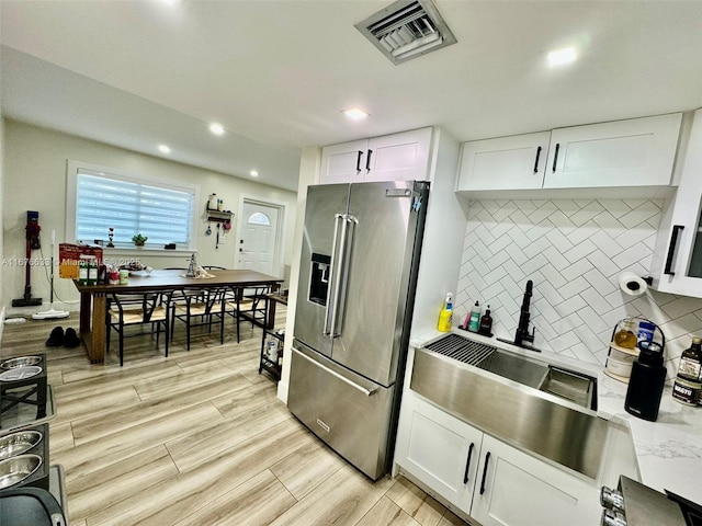 kitchen featuring decorative backsplash, high end refrigerator, white cabinetry, and light hardwood / wood-style flooring