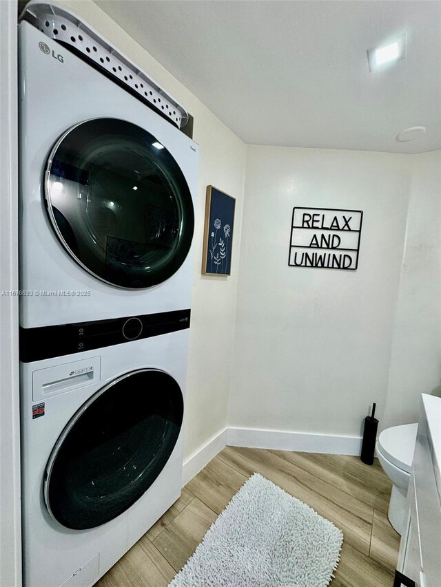 laundry area with light hardwood / wood-style floors and stacked washer and clothes dryer