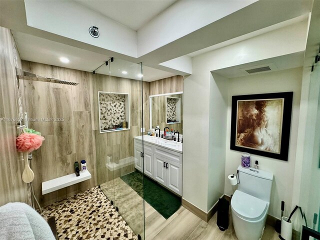 bathroom featuring a tile shower, hardwood / wood-style floors, vanity, and toilet