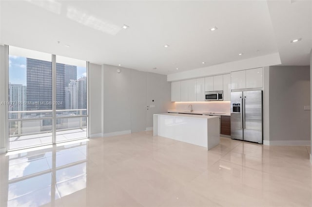 kitchen with appliances with stainless steel finishes, a center island, white cabinetry, expansive windows, and light tile patterned floors