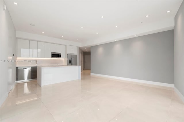 kitchen with white cabinets, light tile patterned floors, appliances with stainless steel finishes, sink, and a center island