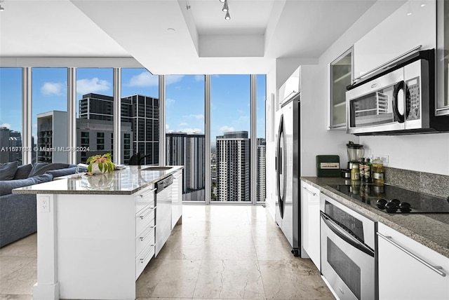 kitchen featuring appliances with stainless steel finishes, expansive windows, white cabinetry, dark stone countertops, and a center island