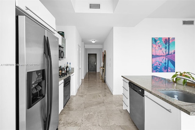 kitchen featuring white cabinets, dark stone countertops, black appliances, and sink