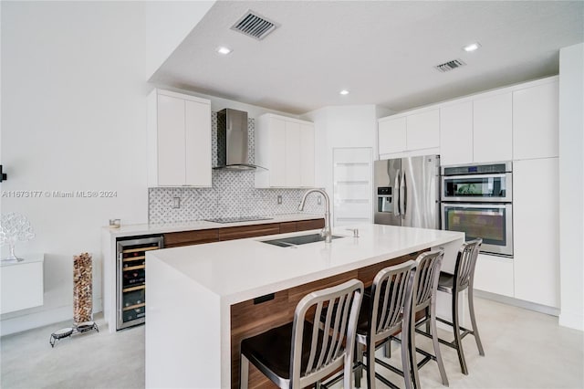 kitchen with sink, wall chimney exhaust hood, stainless steel appliances, beverage cooler, and a center island with sink