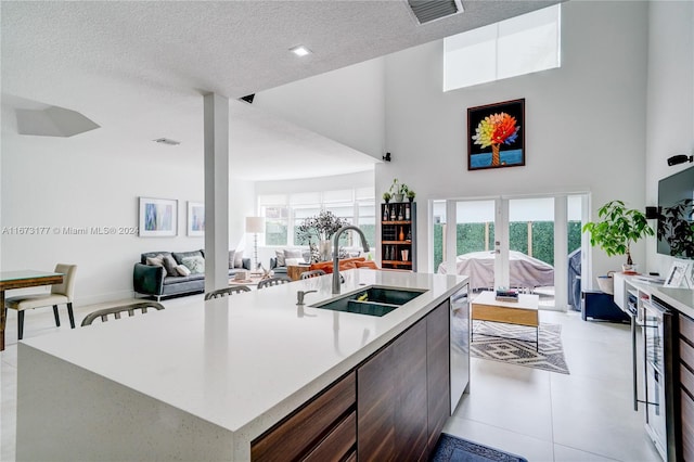 kitchen featuring a textured ceiling, a towering ceiling, sink, and an island with sink