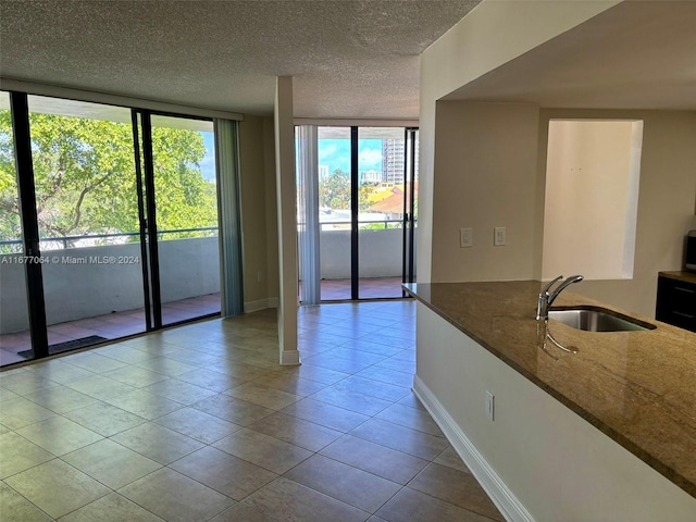 empty room featuring light tile patterned flooring, a textured ceiling, sink, and floor to ceiling windows