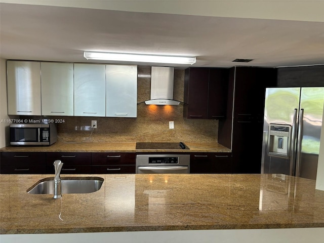 kitchen featuring appliances with stainless steel finishes, wall chimney exhaust hood, sink, and light stone counters