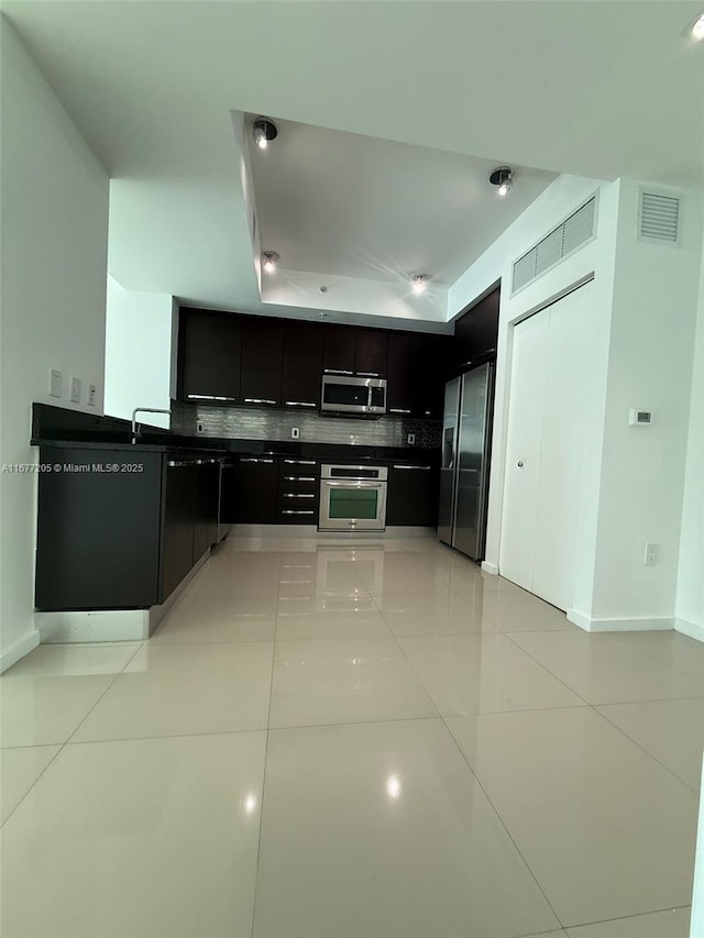 kitchen with stainless steel appliances, a tray ceiling, decorative backsplash, and light tile patterned floors