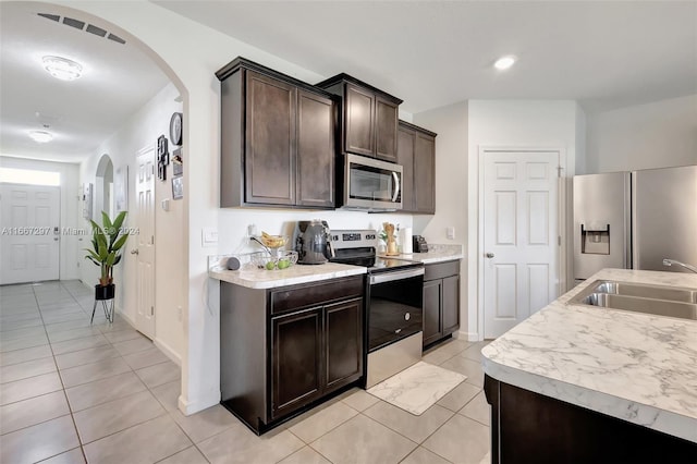 kitchen with sink, appliances with stainless steel finishes, dark brown cabinetry, and light tile patterned floors