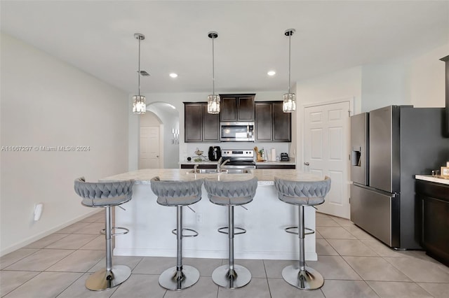 kitchen with a kitchen island with sink, hanging light fixtures, dark brown cabinets, sink, and appliances with stainless steel finishes