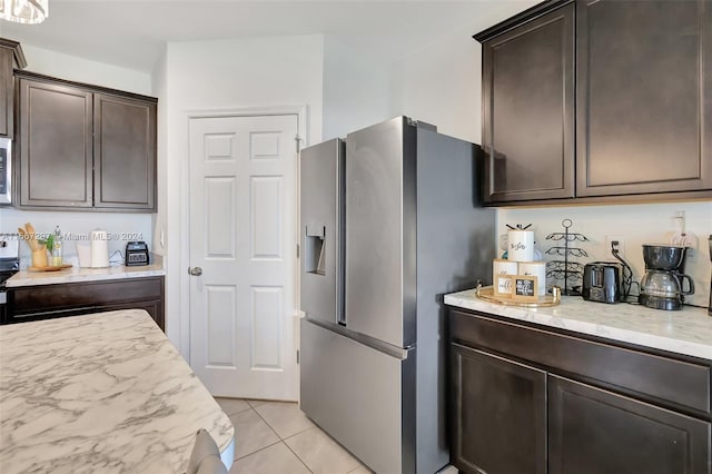 kitchen featuring light stone counters, dark brown cabinetry, stainless steel appliances, and light tile patterned floors