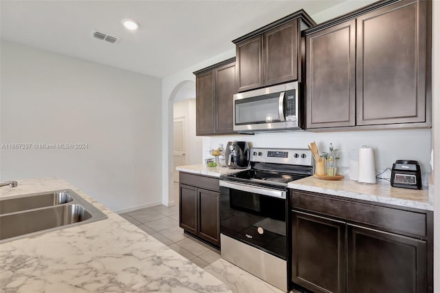 729 SW Lakehurst Dr, Port St Lucie, FL 34983 - kitchen featuring appliances with stainless steel finishes, a sink, arched walkways, dark brown cabinets, and light stone countertops