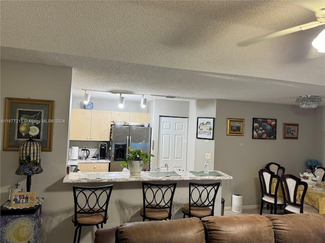 kitchen with light brown cabinetry, a textured ceiling, a kitchen bar, and stainless steel fridge