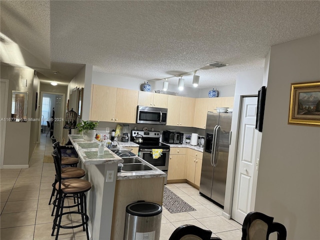 kitchen featuring a breakfast bar area, appliances with stainless steel finishes, a textured ceiling, and light tile patterned flooring