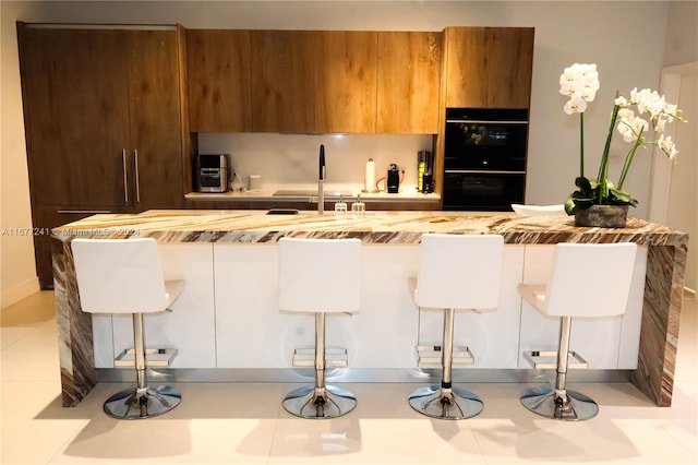 kitchen with light tile patterned flooring, a breakfast bar, double oven, and sink